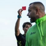 A man in a green hoodie holding up a red card